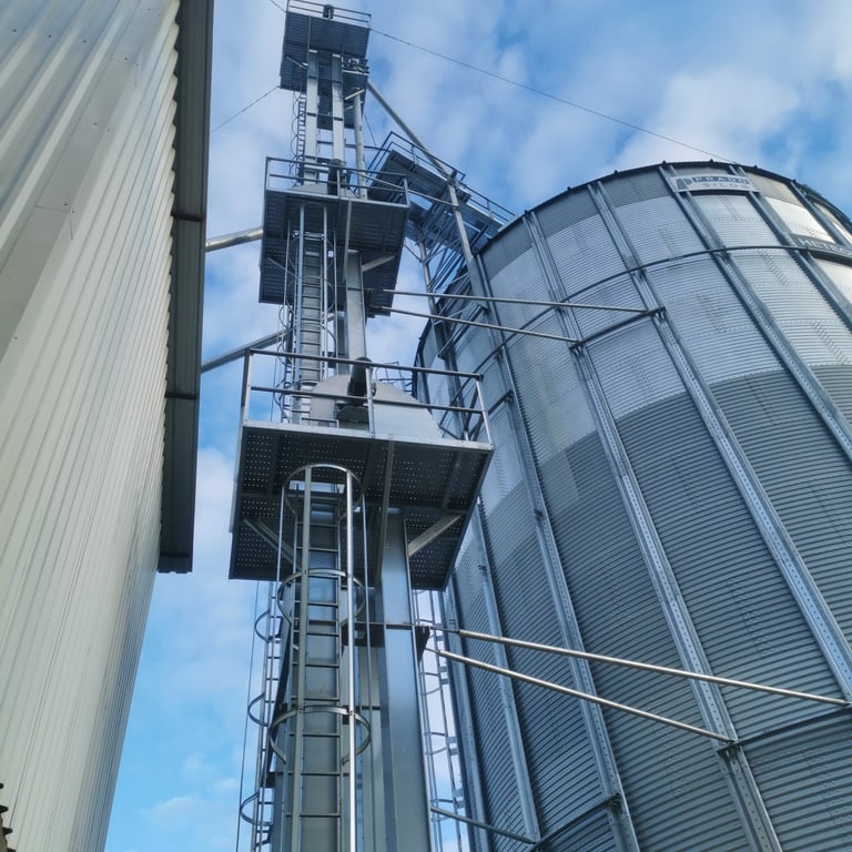 Industrial grain storage silos and metal tower structure against blue sky with clouds