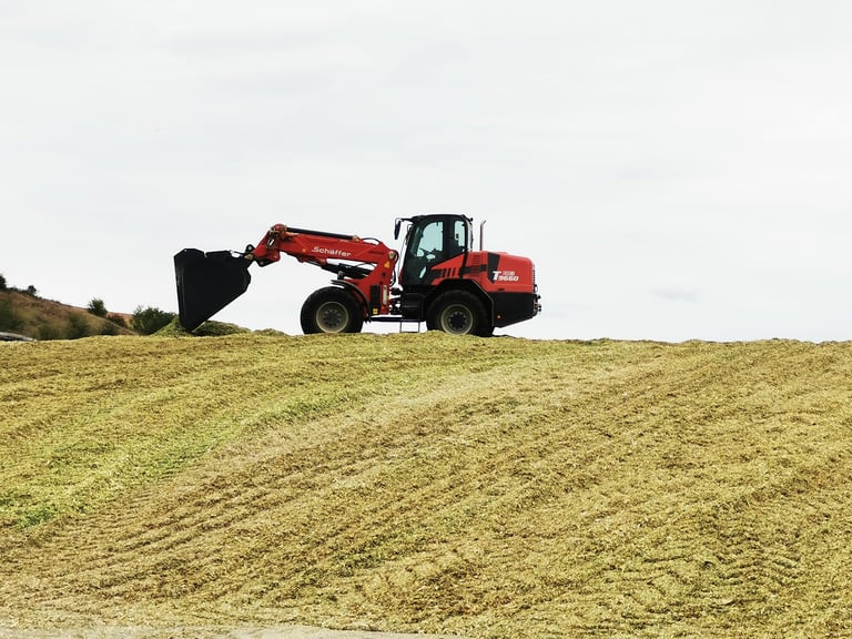 Red and black wheeled excavator operating on farmland, digging into plowed earth under overcast sky
