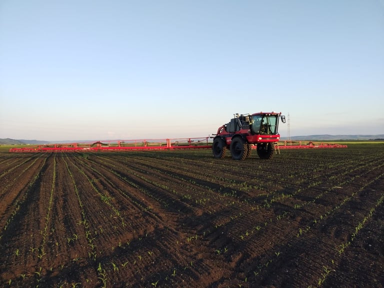 Red and green farm tractor with fertilizer spreader in furrowed field during harvest season